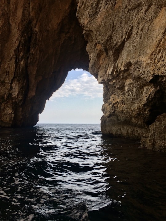 brown rock formation on sea during daytime in Blue Grotto Malta