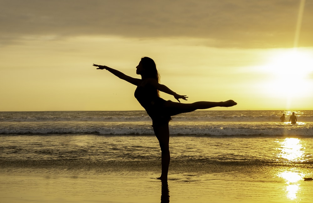 silhouette of woman standing on seashore during sunset