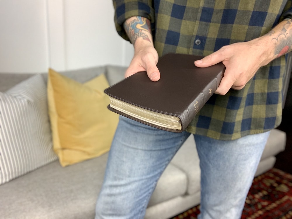 person in blue denim jeans holding black book
