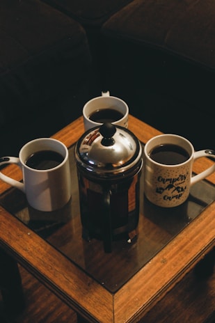 A classic French press filled with rich, dark coffee on a wooden table.