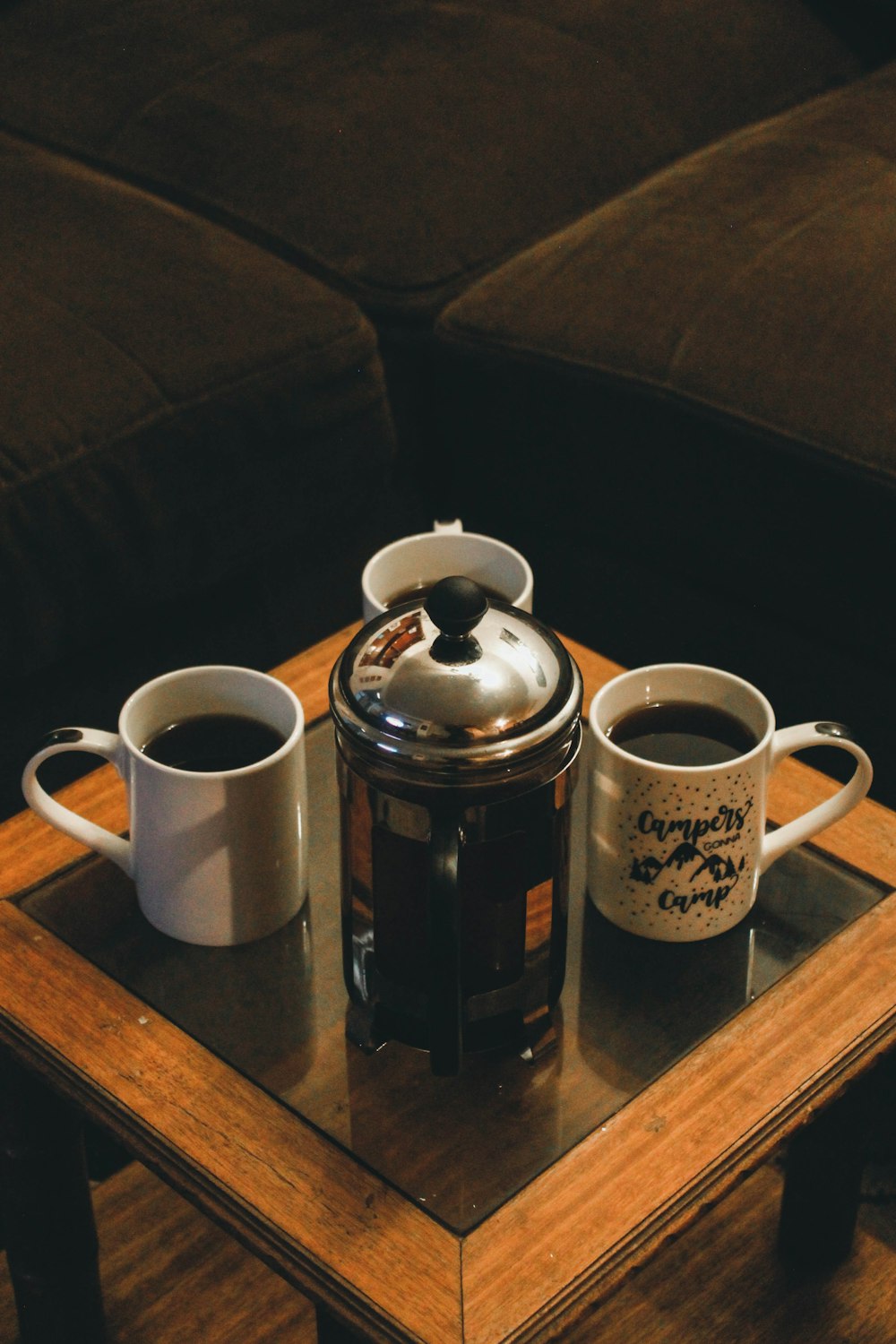 caneca de cerâmica branca ao lado do bule de aço inoxidável na mesa de madeira marrom