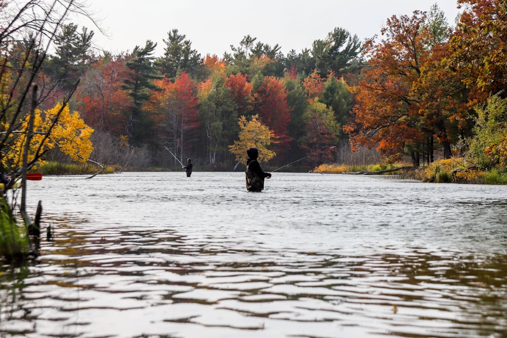 person in black jacket sitting on brown rock in the middle of lake during daytime