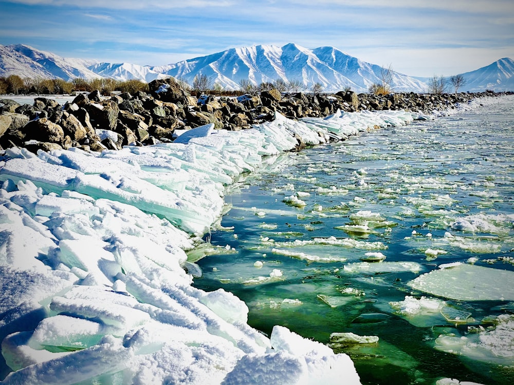 rocky mountain covered with snow near body of water during daytime