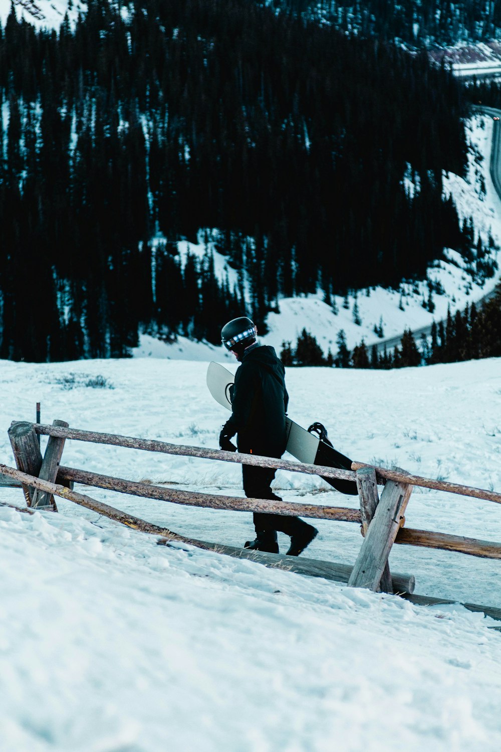 man in black jacket and black pants sitting on brown wooden fence on snow covered ground
