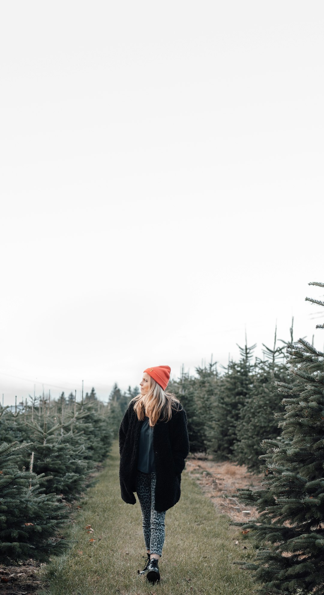 woman in black jacket wearing red knit cap standing on green grass field during daytime