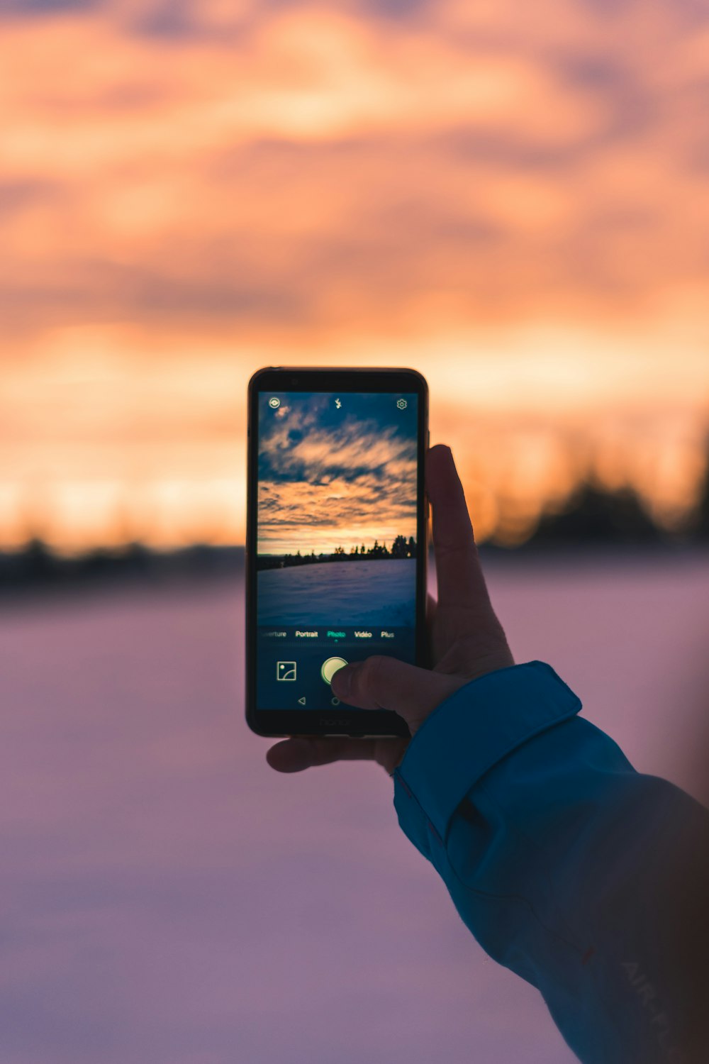 Person mit schwarzem Smartphone beim Fotografieren des Sonnenuntergangs