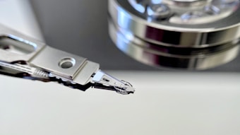 The image captures a close-up view of a hard drive's read/write head alongside a stack of platters. The metallic surfaces and intricate mechanical components are prominently displayed, showcasing the precision engineering of the device.