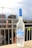 A bottle of Grey Goose vodka is positioned on a ledge with an urban backdrop featuring construction cranes and buildings. The bottle has a frosted appearance with a blue cap and is adorned with images of geese in flight.