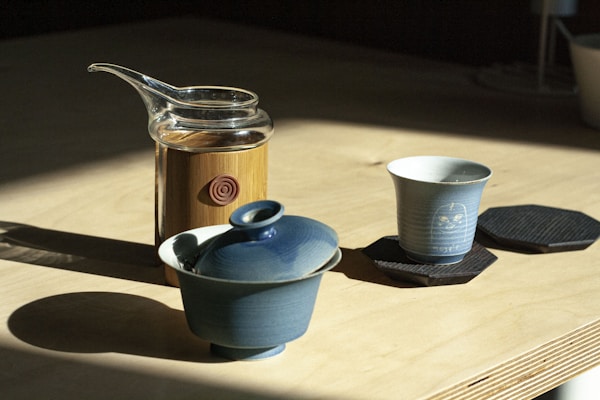 Blue ceramic teapot beside white ceramic mug on brown wooden table