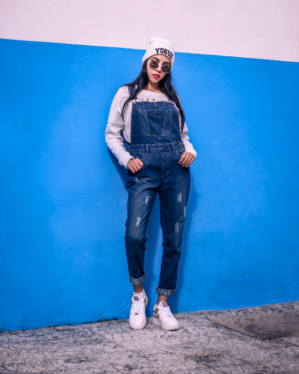 mulher no colete jeans azul e jeans jeans azuis de pé ao lado da parede pintada azul