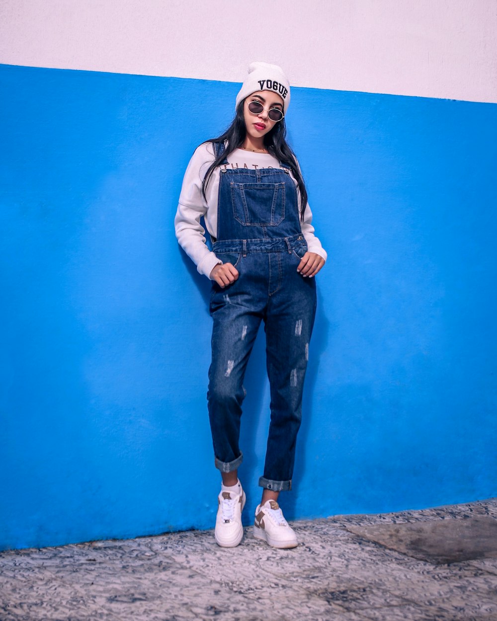 woman in blue denim vest and blue denim jeans standing beside blue painted wall