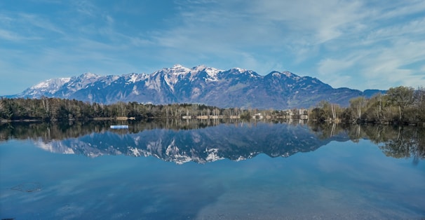 A serene lake reflecting snow-capped mountains during early morning light.