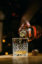 person holding clear drinking glass with brown liquid