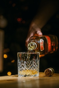 person holding clear drinking glass with brown liquid