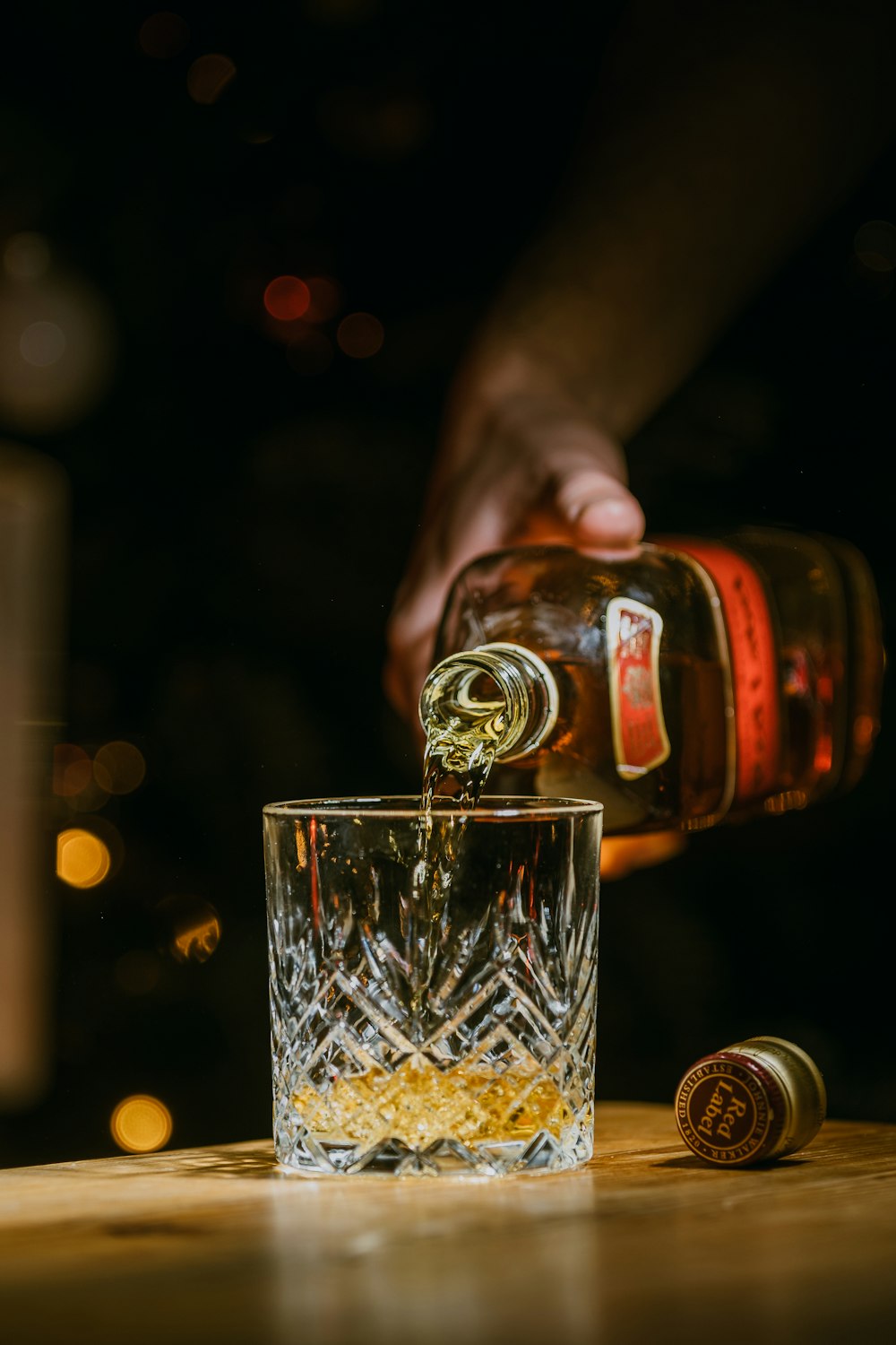 person holding clear drinking glass with brown liquid