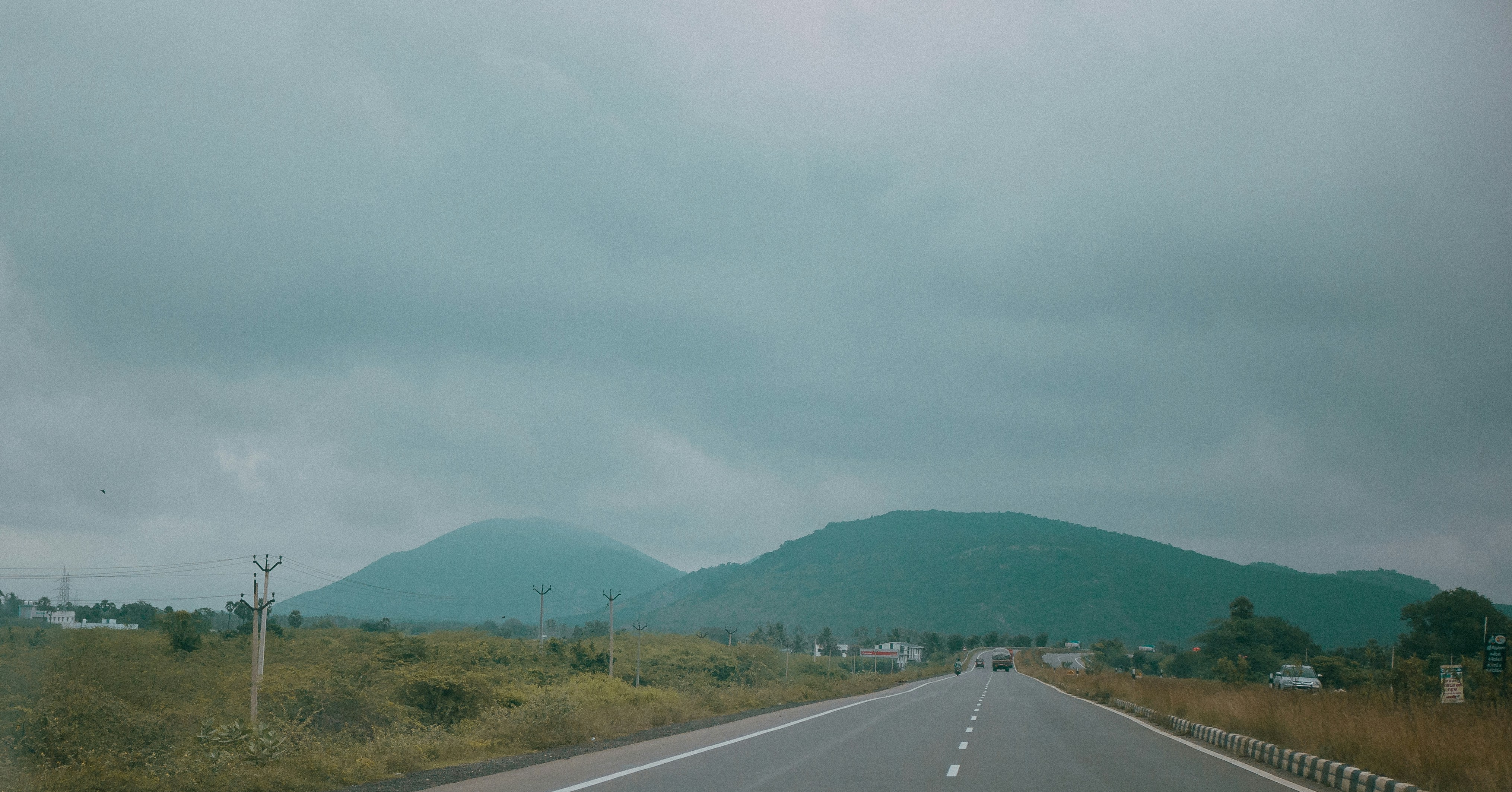 gray concrete road near green mountain under white sky during daytime