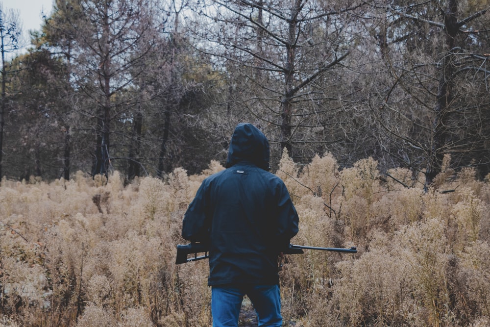 uomo in giacca nera e jeans blu in denim in piedi sul campo di erba marrone durante il giorno