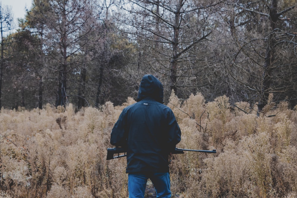 man in black jacket and blue denim jeans standing on brown grass field during daytime