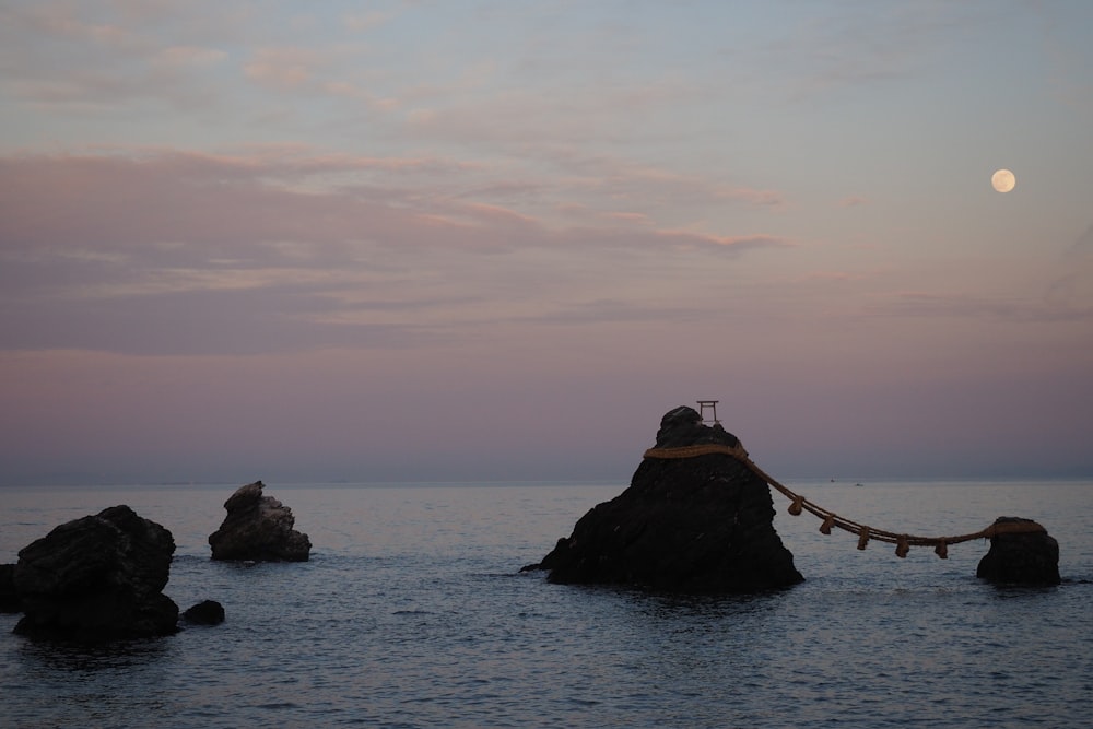 silhouette of person standing on rock formation in the middle of sea during daytime