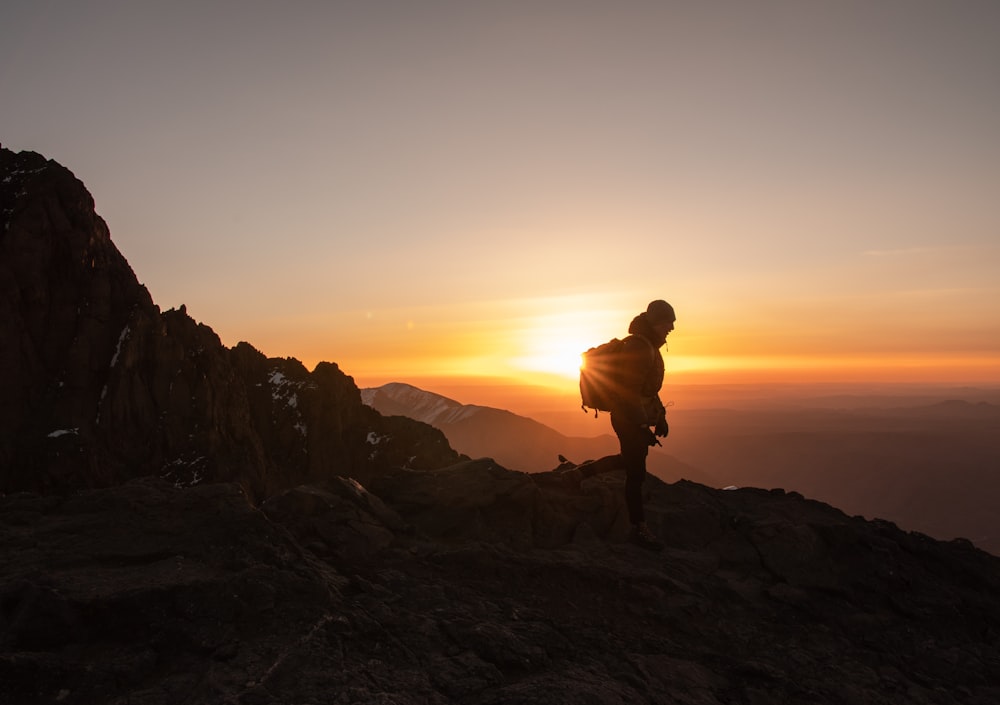 silhouette dell'uomo in piedi sulla formazione rocciosa durante il tramonto