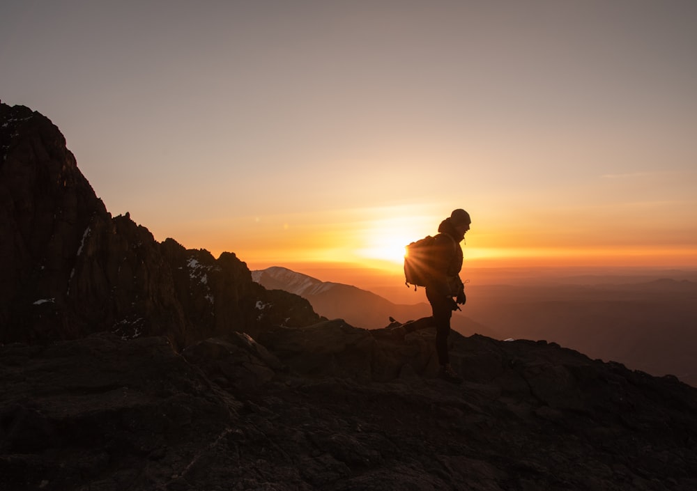 silhouette of man standing on rock formation during sunset