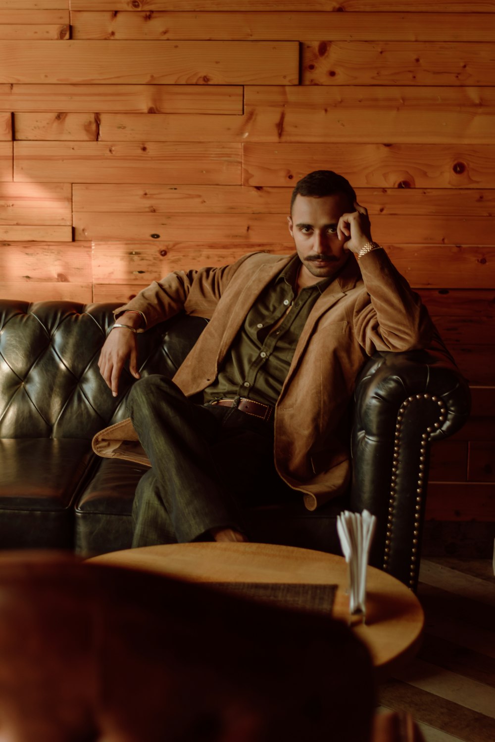 man in brown leather jacket sitting on black leather couch