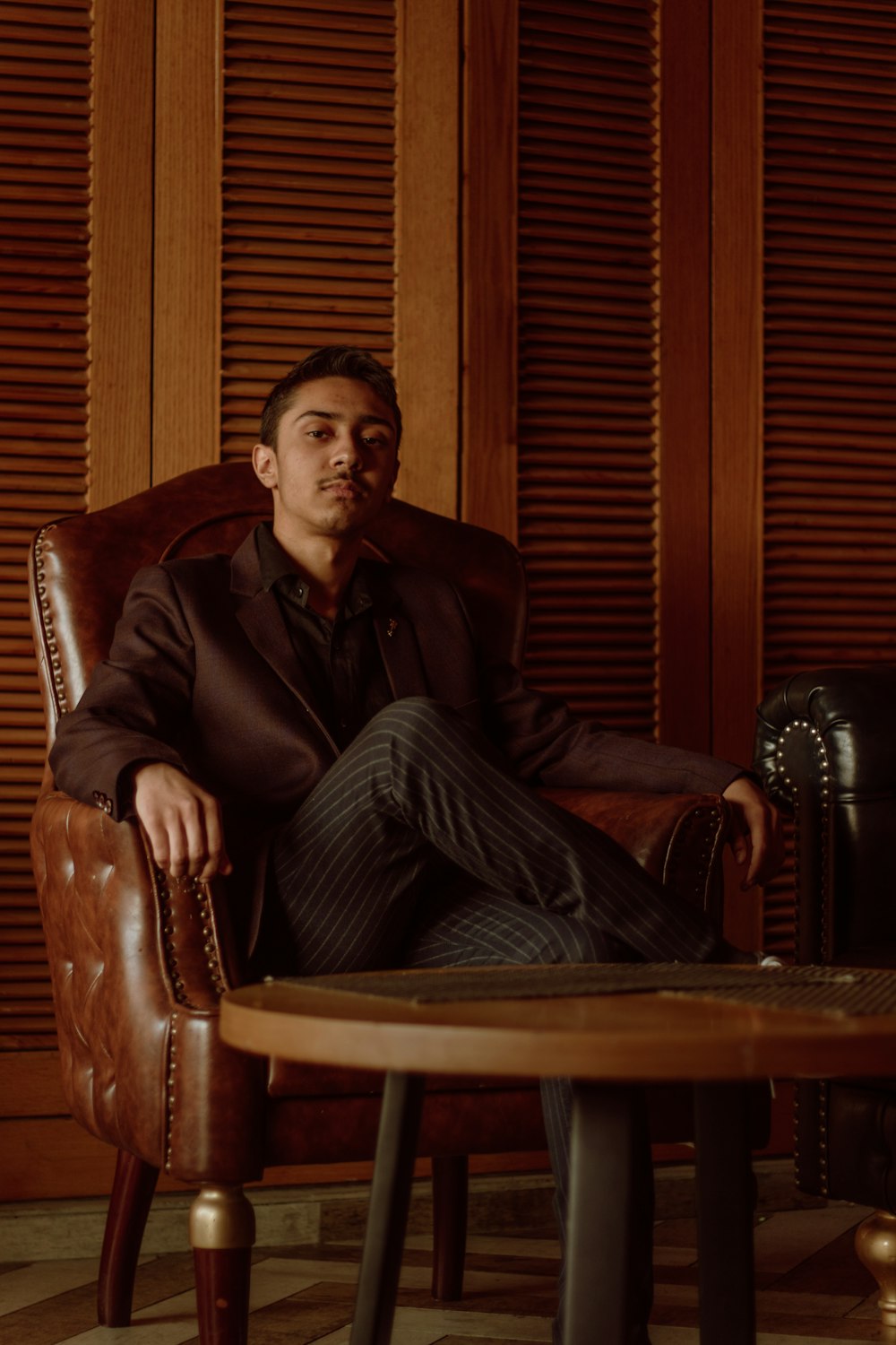 Hombre con chaqueta de cuero negro sentado en un sillón de cuero marrón