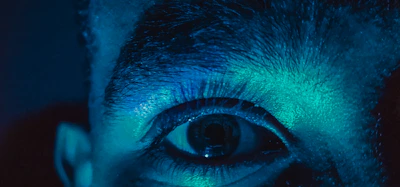 Close-up of a cybernetic eye emitting a bright red glow with subtle neon reflections.