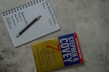 A top view of a notebook open to a page with the headings 'The Weekly Worksheet,' 'Roles,' and 'Goals' written at the top. Each column lists aspects like spiritual, physical, mental, and social/emotional, along with a central note 'Sharpen the Saw.' A pen rests diagonally across the page. Next to the notebook is the book 'The 7 Habits of Highly Effective People' by Stephen R. Covey, placed on a textured gray surface.