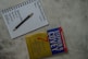 A top view of a notebook open to a page with the headings 'The Weekly Worksheet,' 'Roles,' and 'Goals' written at the top. Each column lists aspects like spiritual, physical, mental, and social/emotional, along with a central note 'Sharpen the Saw.' A pen rests diagonally across the page. Next to the notebook is the book 'The 7 Habits of Highly Effective People' by Stephen R. Covey, placed on a textured gray surface.