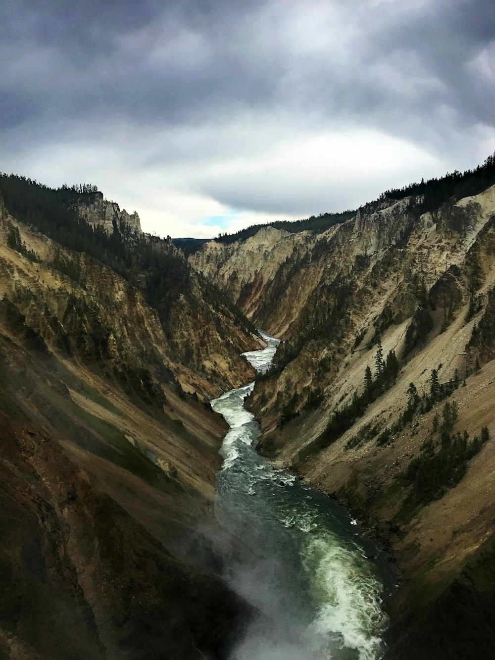 river between brown and green mountains under white clouds during daytime