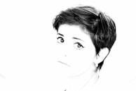 A high-contrast black and white portrait of fer moraga in thoughtful pose against a minimalist background.