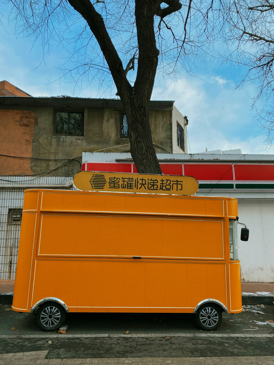 yellow and red bus parked beside brown tree during daytime