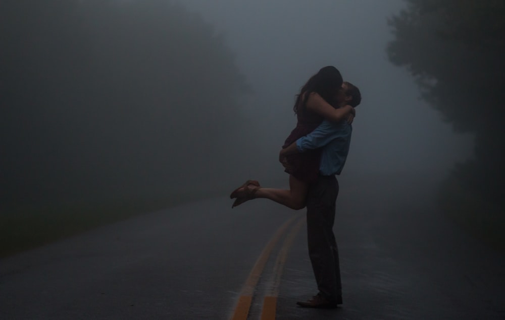 man in blue shirt and black pants holding woman in white shirt