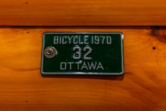 A green vintage bicycle license plate from 1970 with the number 32 and the city name Ottawa is mounted on a wooden surface.
