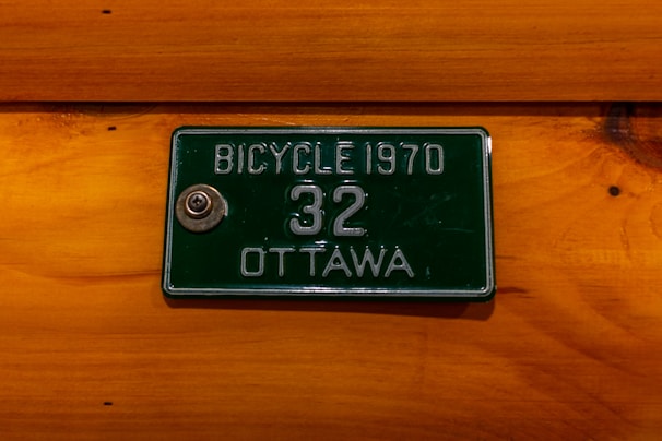 A green vintage bicycle license plate from 1970 with the number 32 and the city name Ottawa is mounted on a wooden surface.