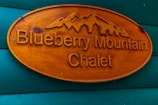 Wooden sign with carved text and mountain design, reading 'Blueberry Mountain Chalet,' mounted on a wall painted in teal.