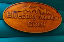 Wooden sign with carved text and mountain design, reading 'Blueberry Mountain Chalet,' mounted on a wall painted in teal.
