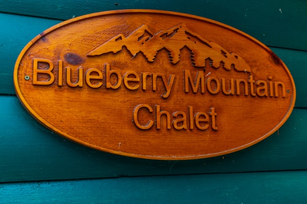 Wooden sign with carved text and mountain design, reading 'Blueberry Mountain Chalet,' mounted on a wall painted in teal.