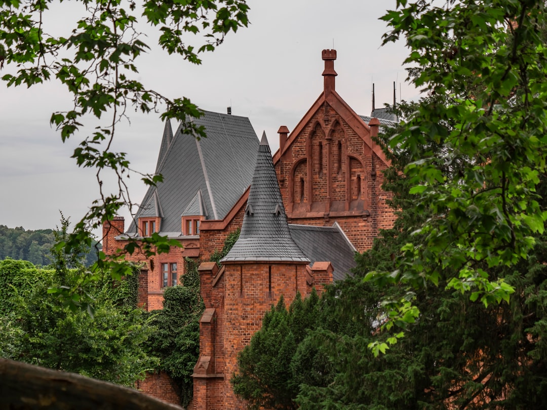 brown brick building near green trees under white clouds during daytime