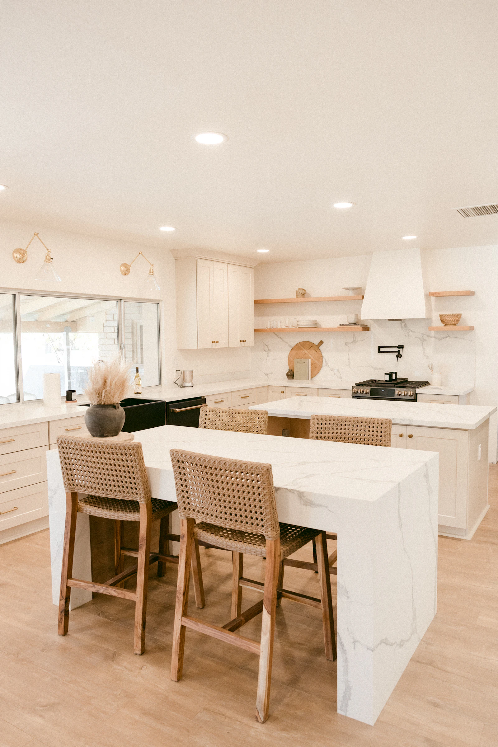 Renovated kitchen with a white marble island, woven bar stools and light wood flooring