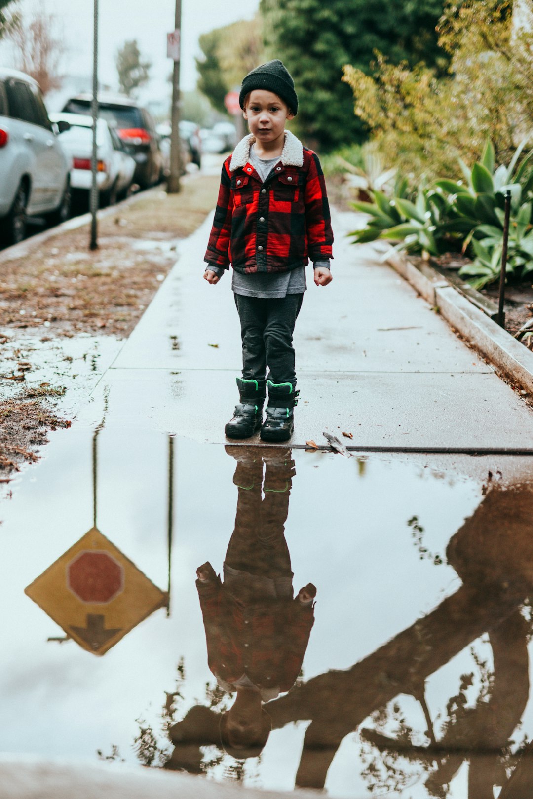 person in red and black jacket and gray pants standing on wet road during daytime