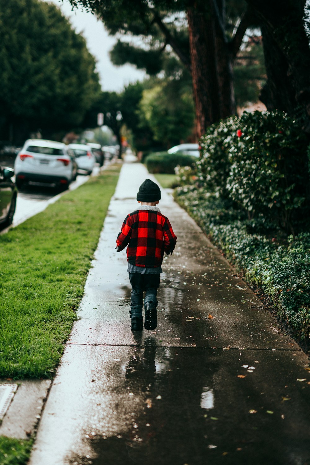 child in red jacket walking on sidewalk during daytime