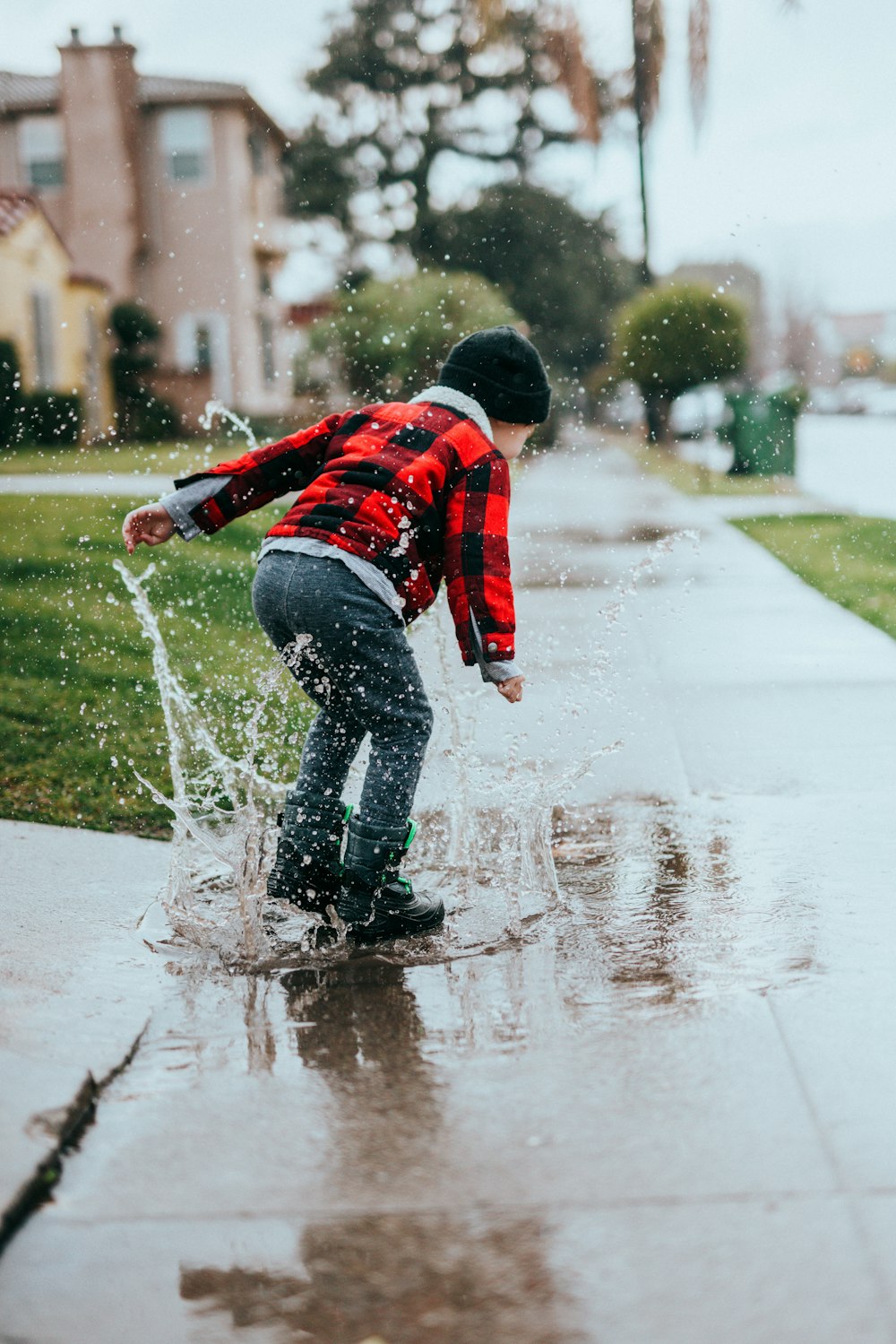 boy in red and black jacket and blue denim jeans playing on water during daytime