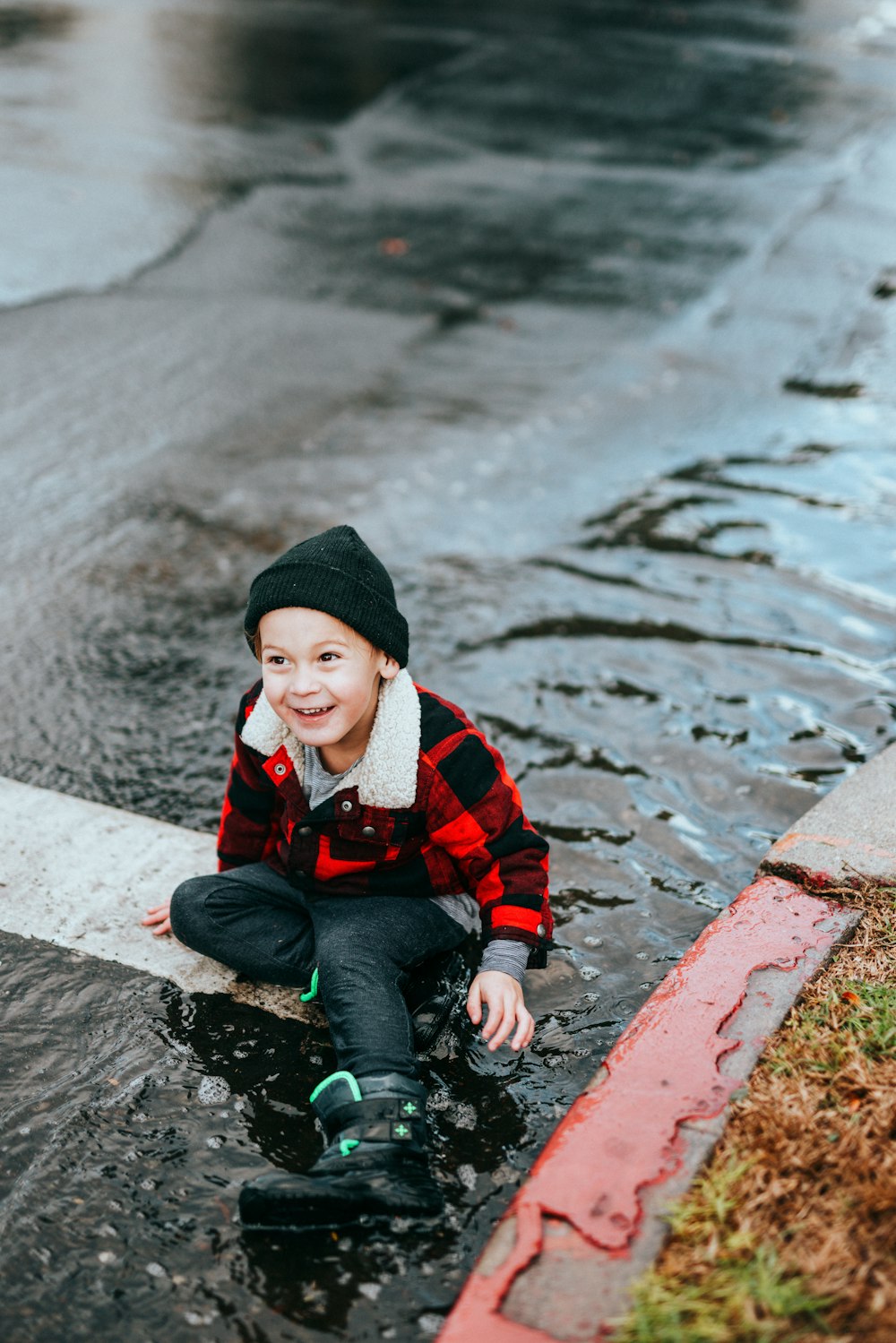 boy in red and black jacket sitting on concrete pavement