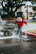 boy in red and black jacket and black knit cap running on wet road during daytime