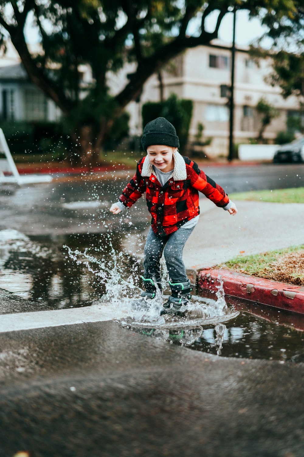 Junge in rot-schwarzer Jacke und schwarzer Strickmütze läuft tagsüber auf nasser Straße