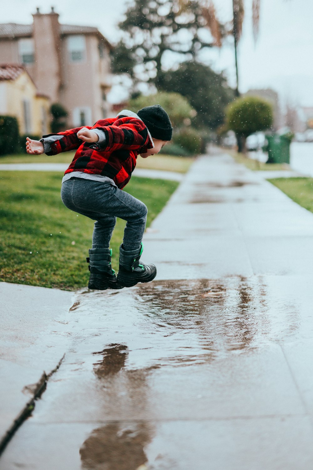 child in red and black jacket and blue denim jeans walking on wet road during daytime