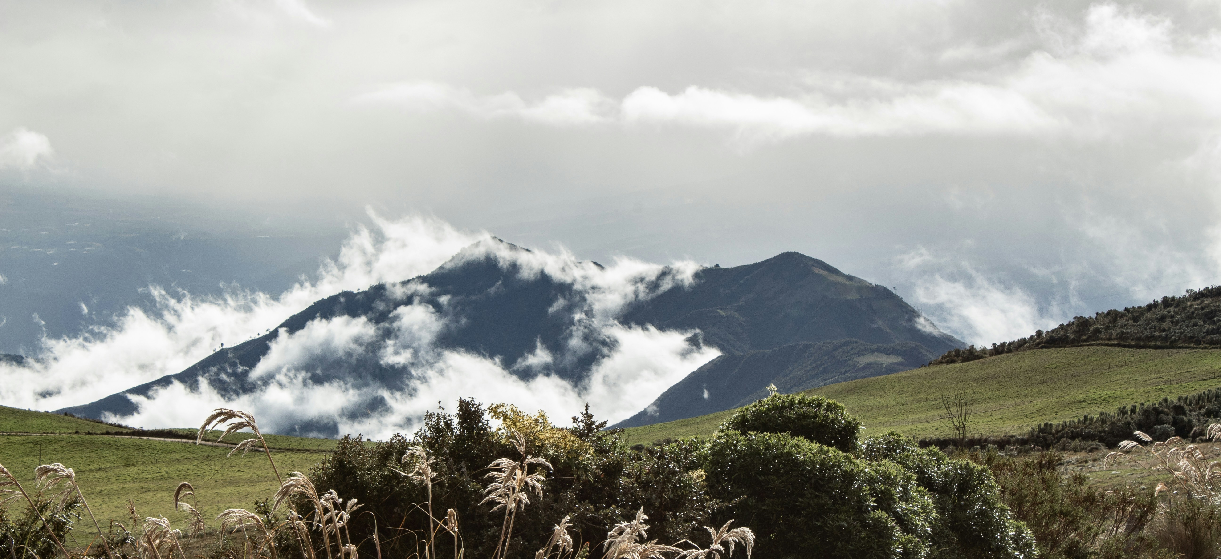 green grass field near mountain under white clouds during daytime