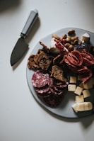 An elegant party platter showcasing rolled deli meats, olives, nuts, and artisan crackers on a rustic table.